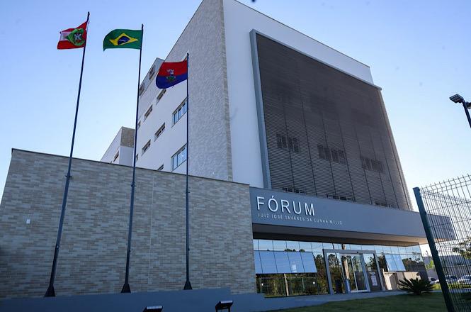 Foto horizontal: fachada do Fórum Juiz José Tavares da Cunha Mello, com bandeiras hasteadas e arquitetura moderna em destaque.