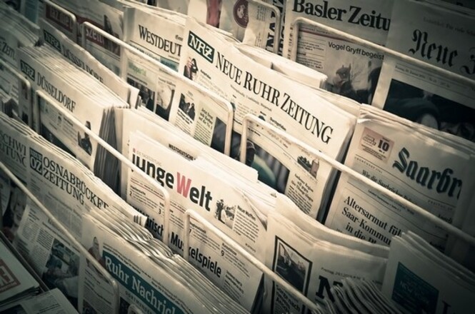 Foto ilustrativa: exemplares de jornais organizados em banca, representando imprensa, circulação de notícias e produção jornalística.