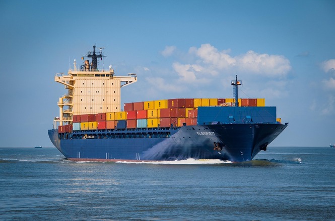 Foto ilustrativa: navio cargueiro transporta contêineres em rota marítima, simbolizando comércio internacional, logística portuária e transporte de cargas.