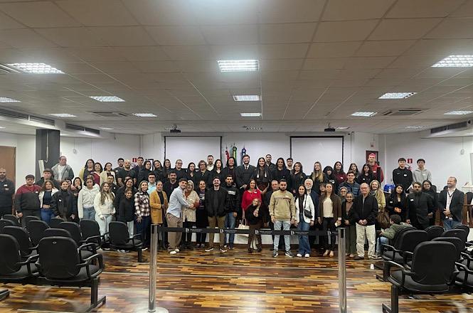 Foto horizontal: participantes de programa educacional e de inclusão social posam para registro coletivo em auditório após atividade de formação e acolhimento.