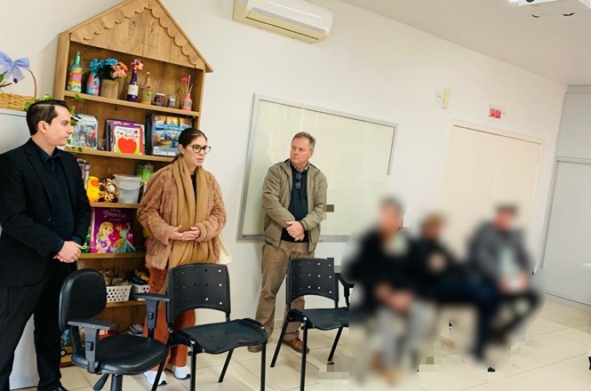 Foto horizontal: representantes do Poder Judiciário conversam com adolescentes em espaço de acolhimento, cercados por livros, brinquedos e materiais educativos voltados à infância e juventude.