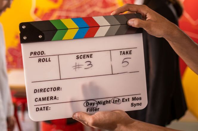 Foto ilustrativa: claquete de cinema é segurada durante gravação audiovisual, simbolizando produção cinematográfica, audiovisual, comunicação e criação de conteúdos.