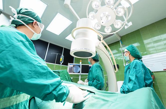 Foto ilustrativa: profissionais da saúde realizam procedimento em centro cirúrgico equipado com tecnologia de imagem, representando atendimento hospitalar, medicina especializada e assistência à saúde.