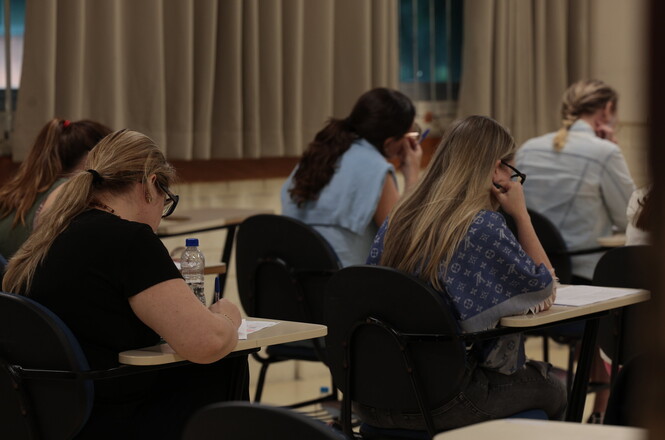 Foto horizontal: participantes realizam atividade avaliativa ou de capacitação em sala de aula, concentrados na leitura e no preenchimento de materiais durante treinamento institucional.