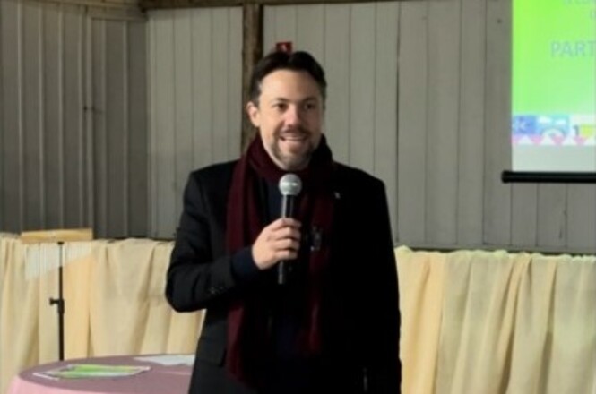 Foto horizontal: magistrado discursa ao microfone durante evento promovido pelo Poder Judiciário, diante de telão de apresentação.