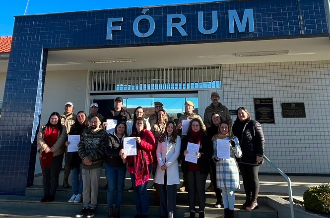 Foto horizontal: representantes de entidades contempladas pelo PJSC Mais Social exibem documentos em frente ao Fórum de Otacílio Costa.