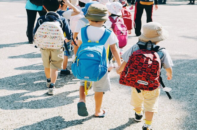 Foto horizontal: crianças caminham com mochilas, representando infância, educação, convivência escolar e desenvolvimento.