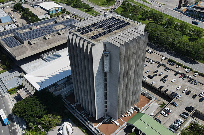 Foto aérea: edifício-sede do Poder Judiciário de Santa Catarina, em Florianópolis, com destaque para a estrutura do tribunal e os painéis de energia solar instalados na cobertura.