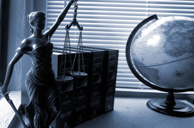 Foto horizontal: estátua da Justiça, códigos jurídicos e globo terrestre simbolizam o Direito, a imparcialidade e a atuação do Poder Judiciário.