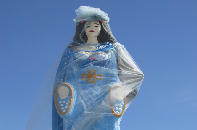 Foto horizontal: imagem de Iemanjá, entidade cultuada nas religiões de matriz africana, ao ar livre sob céu azul.
