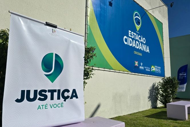Foto horizontal: banner do programa Justiça Até Você em frente à Estação Cidadania, em Criciúma, local de atendimento à população.