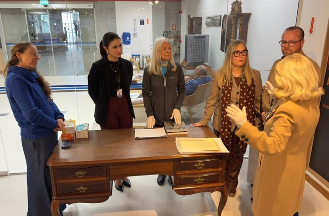 Foto horizontal: grupo acompanha apresentação de documentos históricos durante visita técnica às dependências do fórum.
