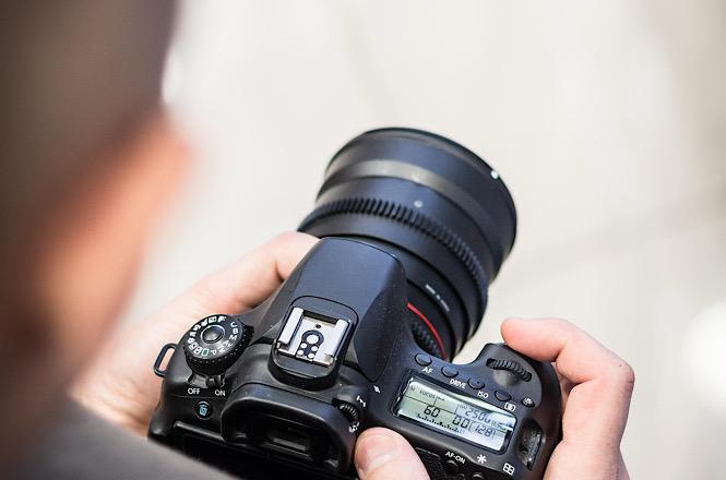 Foto horizontal: mãos seguram câmera fotográfica profissional durante registro de imagens para cobertura jornalística.