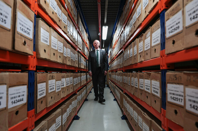 Foto horizontal: desembargador Rubens Schulz caminha entre estantes de arquivos do acervo documental do Poder Judiciário de Santa Catarina.