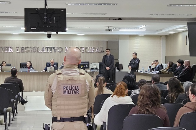 Foto horizontal: policiais militares acompanham audiência no plenário da Câmara de Vereadores, com público e autoridades presentes.
