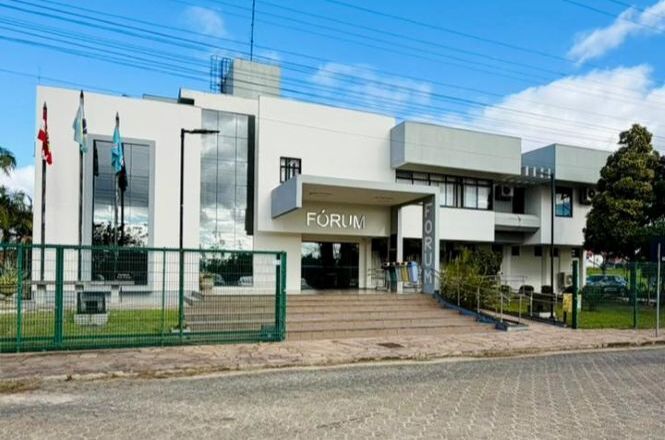 Foto horizontal: fachada do Fórum da comarca, com entrada principal, escadaria, rampa de acessibilidade e área ajardinada.