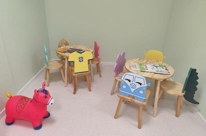Foto horizontal: espaço infantil com mesas, cadeiras temáticas, brinquedos e livros, preparado para acolhimento de crianças no ambiente do fórum.