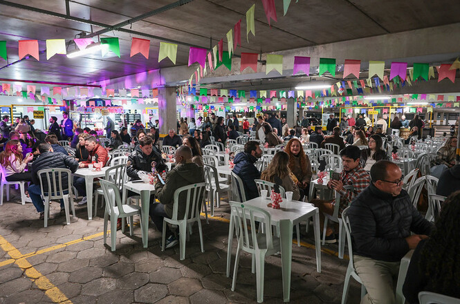 Foto horizontal: participantes ocupam mesas decoradas com bandeirinhas durante festa junina promovida pelo TJSC em ambiente coberto.