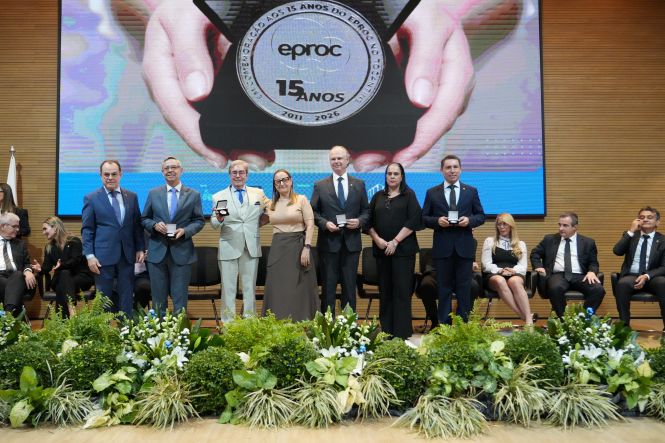 Foto horizontal: autoridades e homenageados posam no palco durante cerimônia em comemoração aos 15 anos do sistema eproc, exibindo medalhas comemorativas diante do painel do evento.