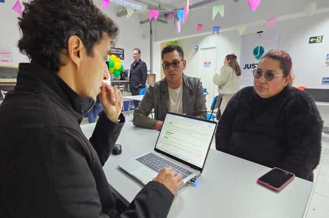 Foto horizontal: servidor atende casal em posto de atendimento itinerante da Justiça, utilizando notebook para prestar orientações e realizar procedimentos administrativos.