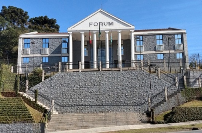 Horizontal: Fachada de fórum com escadaria, colunas, área ajardinada e céu azul em ambiente urbano.