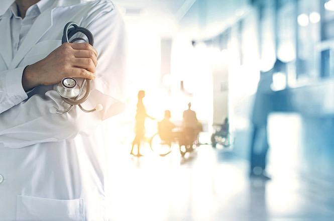 Foto horizontal: profissional de saúde segura um estetoscópio em corredor hospitalar, em imagem ilustrativa que representa atendimento médico, assistência hospitalar e cuidados com a saúde.