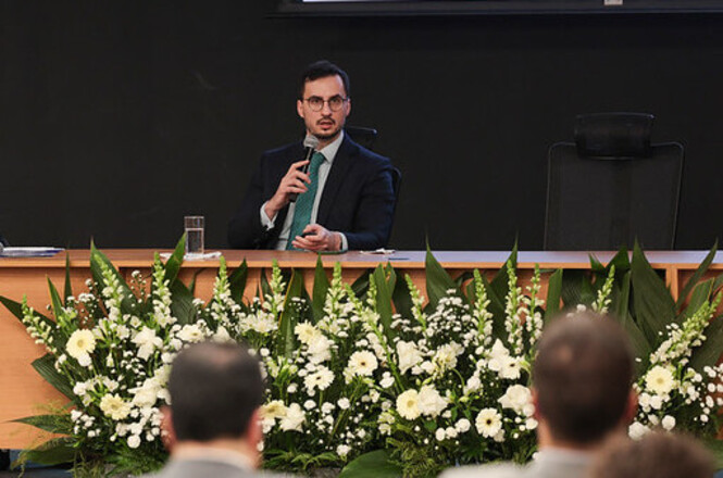 Foto horizontal: palestrante fala ao microfone durante conferência em auditório, apresentando conteúdo técnico ao público em evento institucional do Poder Judiciário.