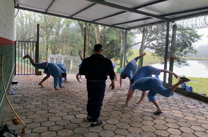 Pessoas privadas de liberdade praticam capoeira durante atividade de ressocialização em unidade prisional.