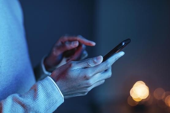 Pessoa utiliza telefone celular em ambiente com pouca luz, em referência ao uso de dispositivos móveis.