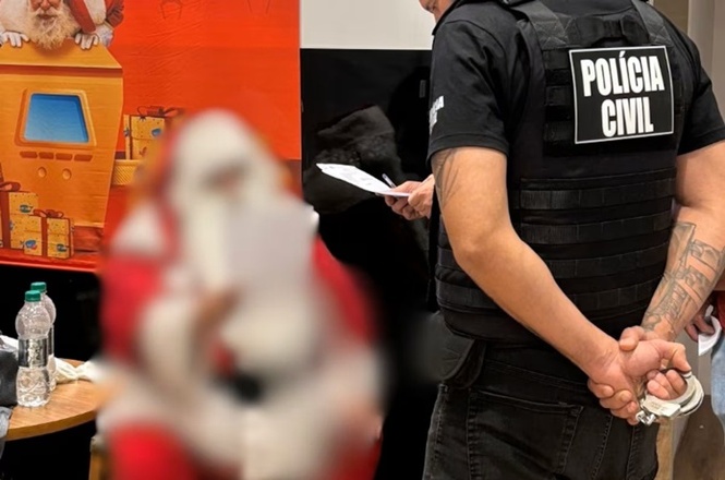 Policial civil cumpre mandado enquanto pessoa vestida de Papai Noel aparece desfocada ao fundo.