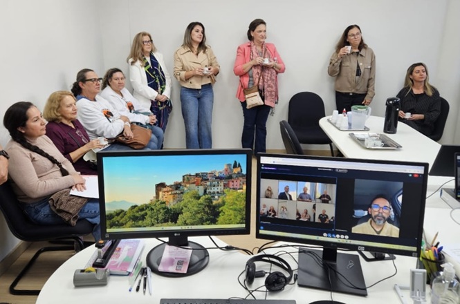 Servidores acompanham videoconferência em sala de reunião durante encontro híbrido de trabalho.