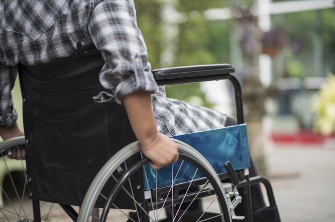 Pessoa conduz cadeira de rodas por área externa, representando mobilidade e acessibilidade para pessoas com deficiência.
