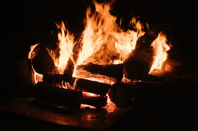 Lenha em chamas aquece lareira, com labaredas intensas iluminando o ambiente escuro.