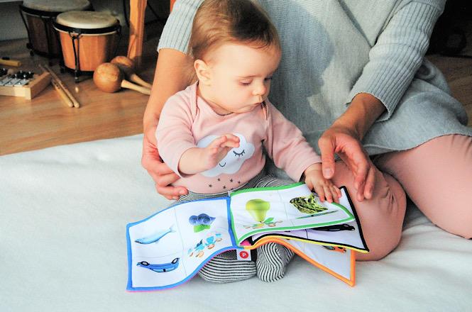 Bebê explora livro ilustrado com apoio de pessoa adulta durante momento de leitura e interação.
