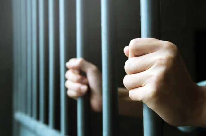 Mãos seguram as grades de uma cela, simbolizando privação de liberdade no sistema prisional.
