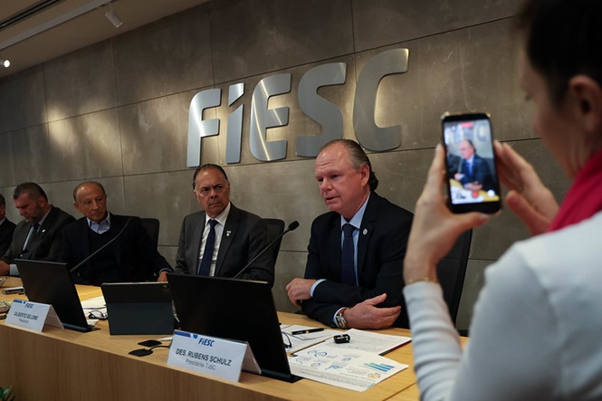 Des. Rubens Schulz participa de reunião na Fiesc enquanto pessoa registra o encontro com um celular.
