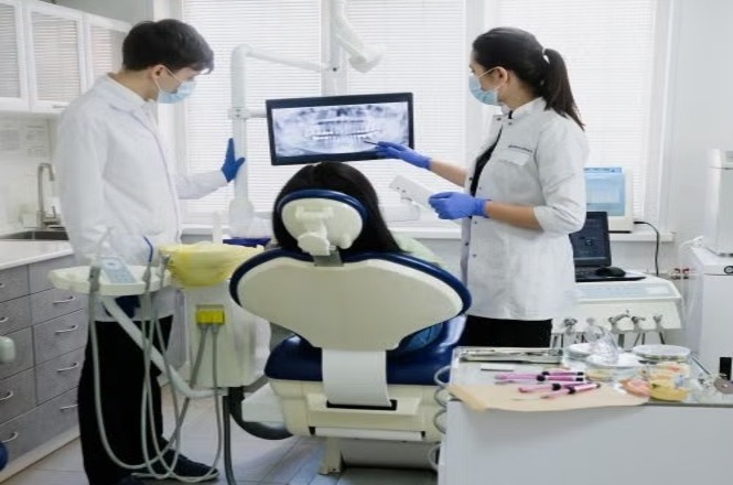 Profissionais de odontologia analisam exame de imagem ao lado de paciente em consultório odontológico.