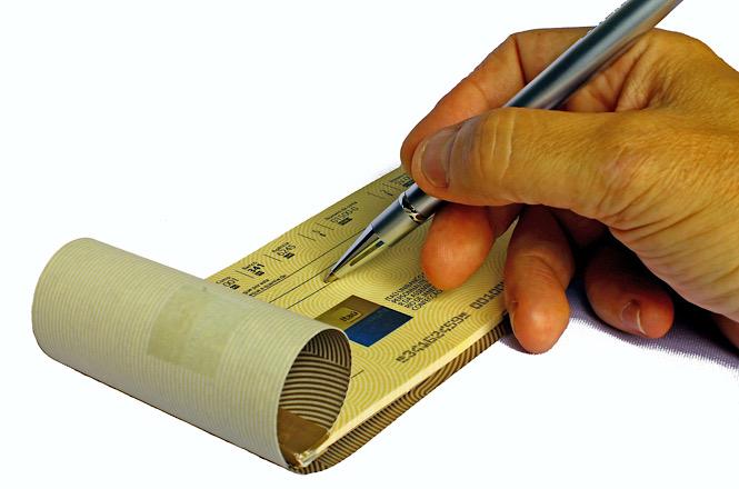 Mão preenche cheque bancário com caneta sobre fundo branco.