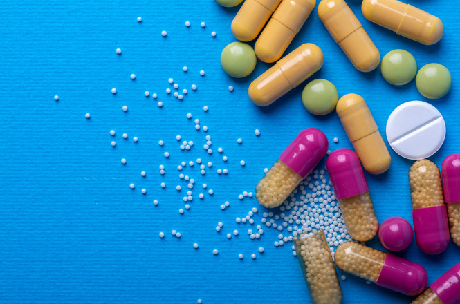 Cápsulas, comprimidos e grânulos coloridos sobre superfície azul, representando medicamentos.