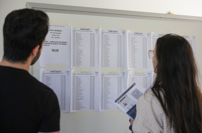 Candidatos consultam lista de aprovados afixada em mural durante processo seletivo.