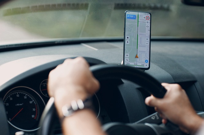 Motorista conduz veículo com aplicativo de navegação exibido em celular fixado ao painel do automóvel.