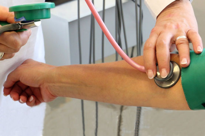 Profissional de saúde afere a pressão arterial de paciente durante atendimento clínico.