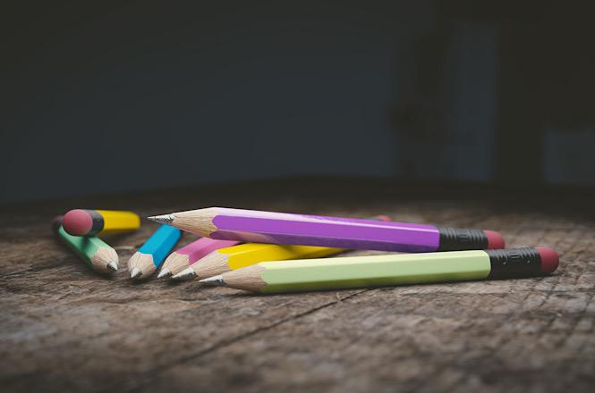 Foto horizontal: Lápis de cor espalhados sobre mesa de madeira simbolizam educação, aprendizagem e desenvolvimento infantil.
