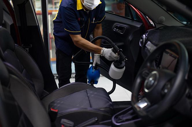 Foto horizontal: Profissional realiza higienização do interior de veículo com equipamento de limpeza e desinfecção.