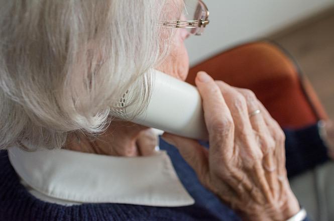 Foto horizontal: pessoa idosa segura um telefone junto ao ouvido durante ligação, em imagem ilustrativa que representa atendimento remoto, comunicação e serviços de apoio à população idosa.