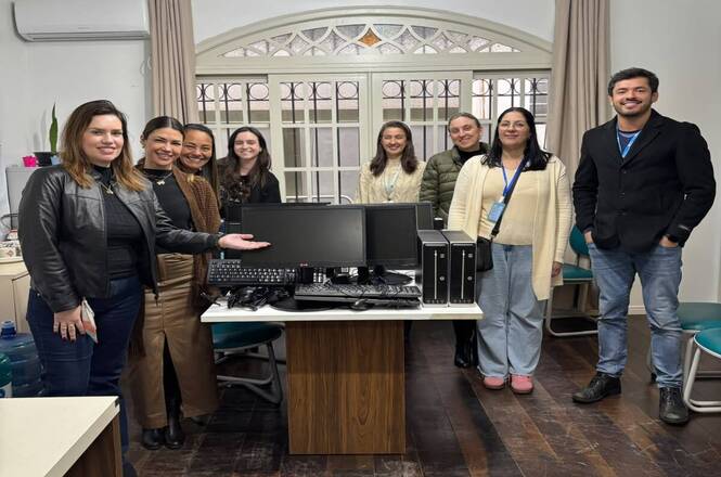 Foto horizontal: equipe de servidores posa ao redor de estação de trabalho equipada com computadores recém-instalados, durante entrega ou modernização de equipamentos em unidade do Poder Judiciário.
