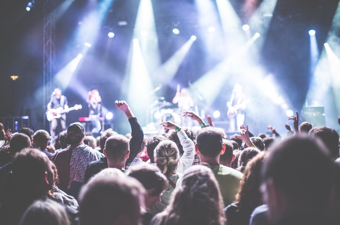 Foto horizontal: público acompanha show com banda em palco iluminado, em imagem ilustrativa que representa eventos musicais e grandes apresentações ao vivo.
