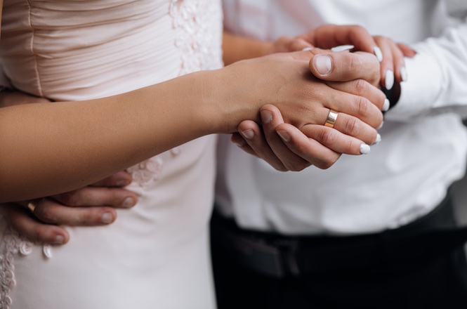 Foto horizontal: close nas mãos de um casal com alianças durante cerimônia de casamento, em imagem ilustrativa que representa união civil, matrimônio e compromisso conjugal.