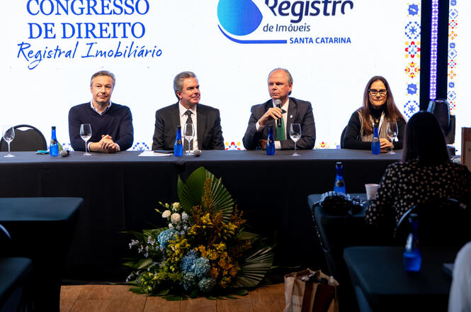 Foto horizontal: mesa de autoridades participa de painel durante o Congresso de Direito Registral Imobiliário. Ao microfone, o desembargador Rubens Schulz conduz sua exposição diante do público.