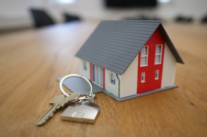 Foto horizontal: Miniatura de casa e chave sobre mesa representam aquisição, financiamento ou regularização de imóvel.